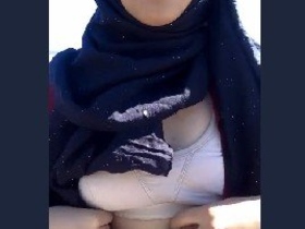 A college girl wearing a hijab reveals her small breasts to her partner in an outdoor setting.